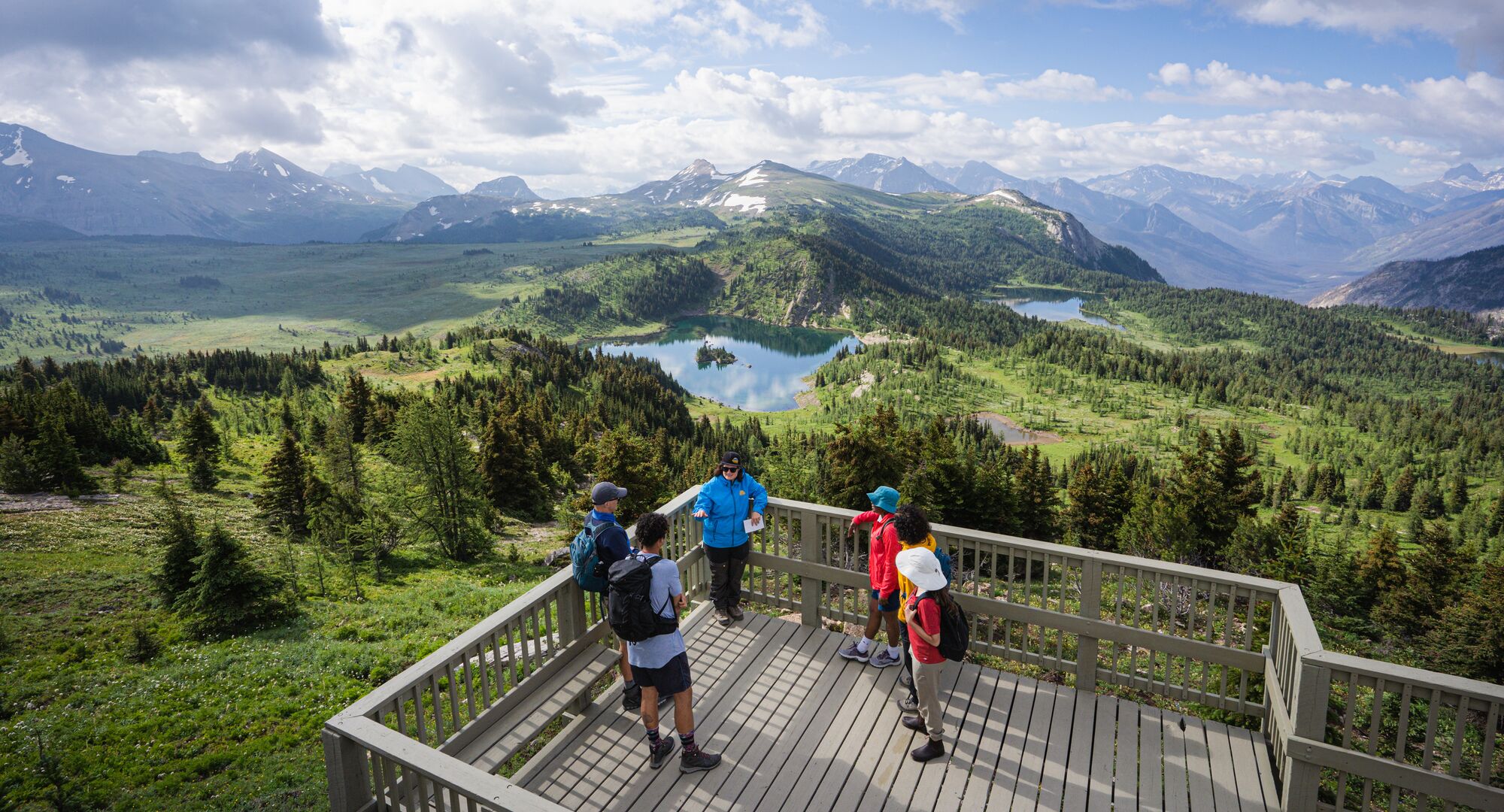 A group of people stand at a viewing deck at Sunshine Meadows overlooking alpine lakes and peaks in Sunshine Meadows